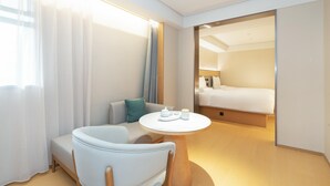 Une chambre d’hôtel moderne avec un canapé, une table ronde agrémentée d’un service à thé et un lit en arrière-plan.