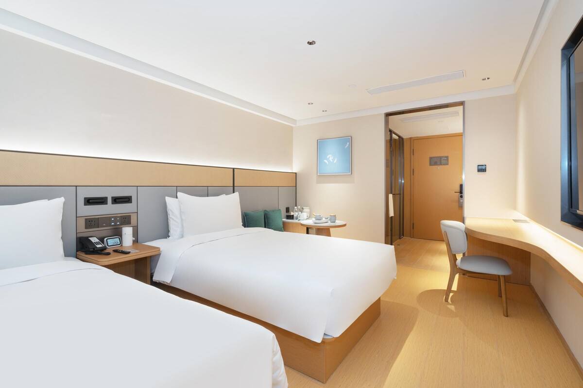Una habitación de hotel con dos camas, un escritorio, una silla, una mesita pequeña y una mesita de noche con teléfono y control remoto.