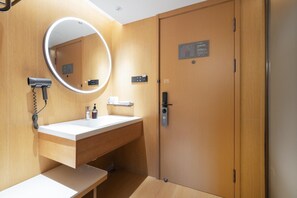 A modern bathroom with a wooden vanity, a round mirror, a hairdryer, and a door with a control panel. - Ji Hotel Guangzhou Jiangtai Road Metro Station (Guangzhou)