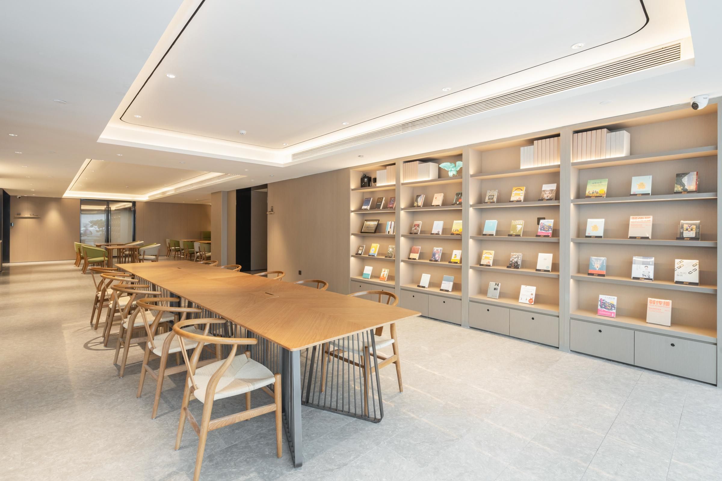 Une bibliothèque moderne avec une longue table en bois et des chaises, entourée d’étagères.