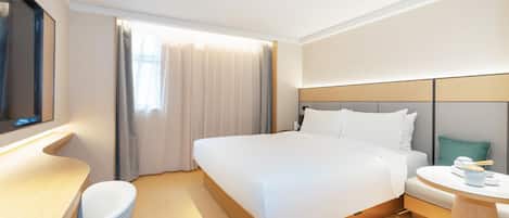 A modern hotel room with a large bed, a desk, and a round table.