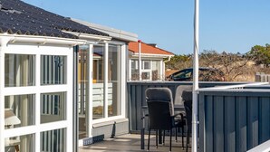Un espacio al aire libre cubierto con una terraza de madera, dos sillas y vista a una casa con techo rojo.