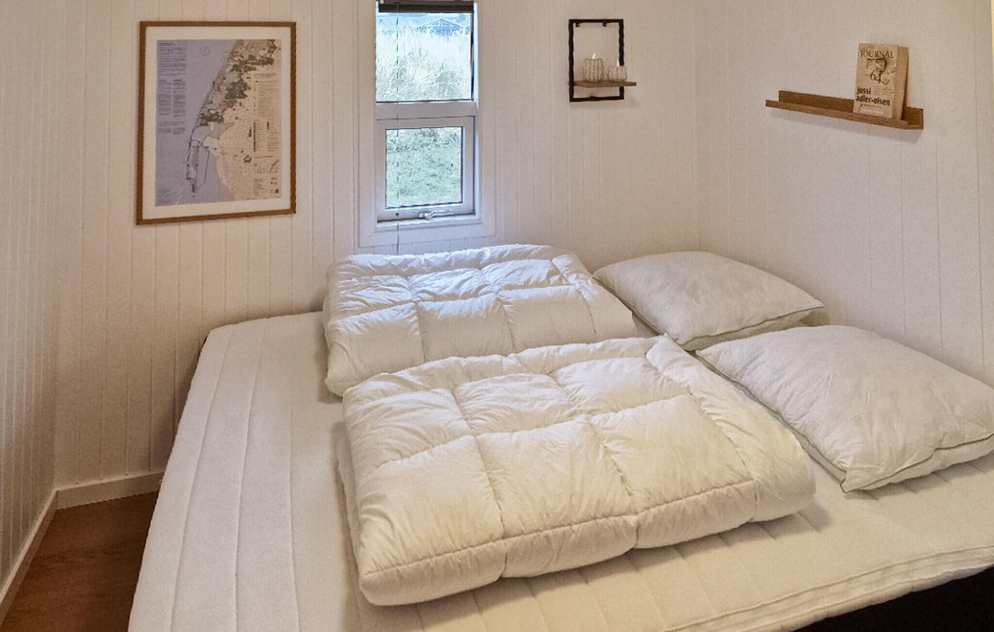 Une chambre à coucher avec un lit, une fenêtre et une étagère fixée au mur, sur laquelle se trouve un livre.