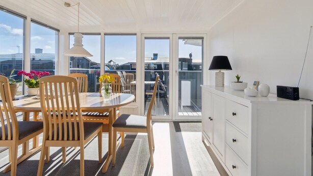 Una habitación luminosa e inundada de sol, con una mesa de comedor de madera, sillas y un armario blanco.
