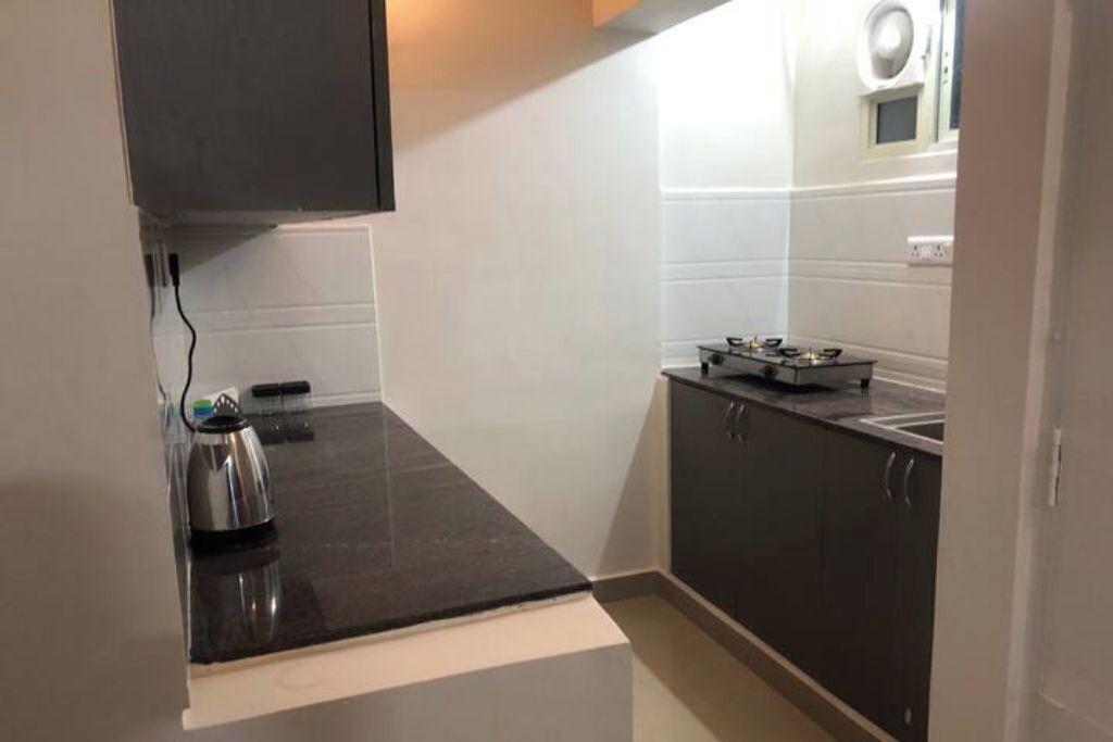 A compact kitchen with dark countertops, a kettle, and a stove.