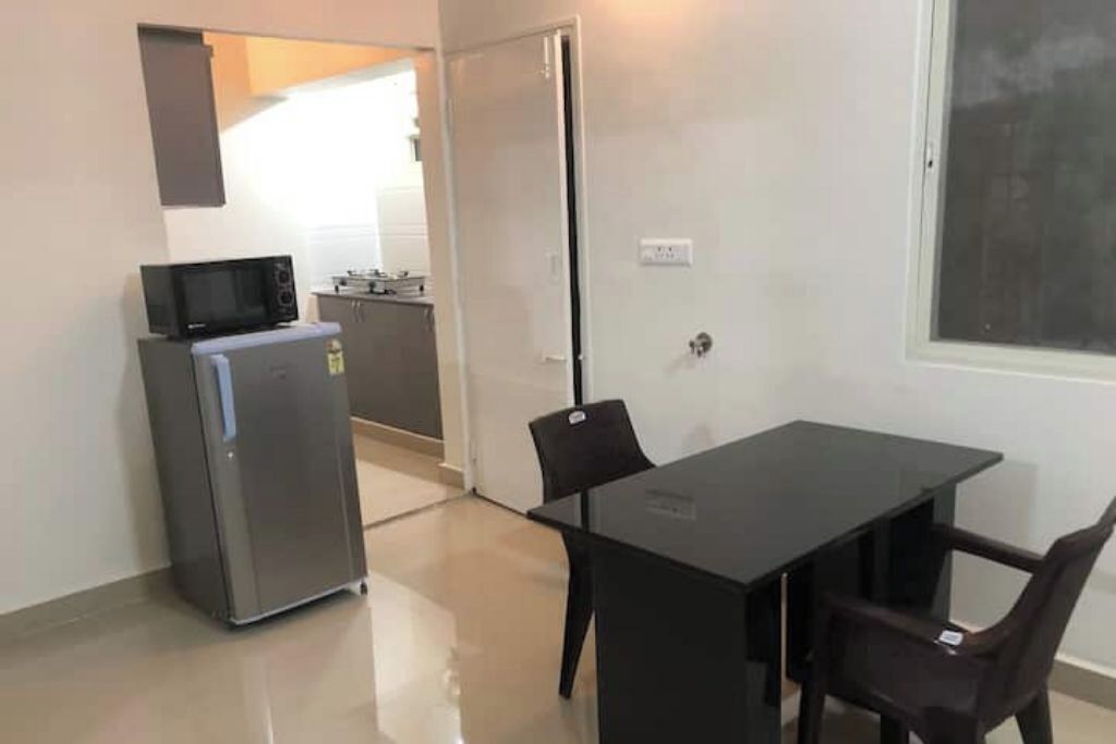 A compact kitchen with a refrigerator, microwave, and cabinets. There is a dining table with chairs.