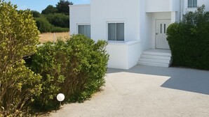 A modern white building with a satellite dish, a gravel driveway, and surrounding greenery. - Aegean Helios Houses (Rhodes)