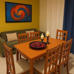 A dining area with a wooden table, four chairs, two candles, and a bowl of dried flowers.
