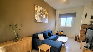 A modern living room with a sectional sofa, a small wooden table, a TV, and a fireplace. - Aegean Helios Houses (Rhodes)