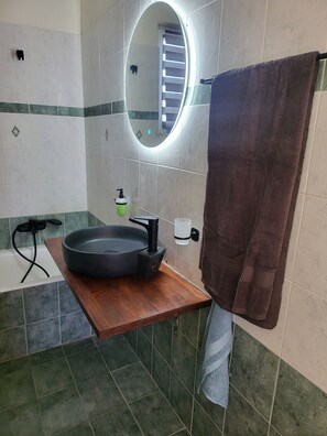 A bathroom with a round mirror, a black basin, a wooden countertop, a towel rack, and a visible staircase in the background.