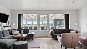 A modern living room with a large window, a flat-screen TV, and a grill outside.