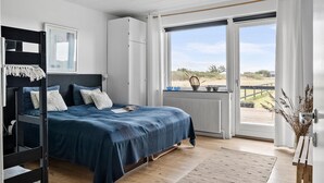 A bedroom with a bunk bed, a large window with a view of the outdoors, and a radiator near the window.