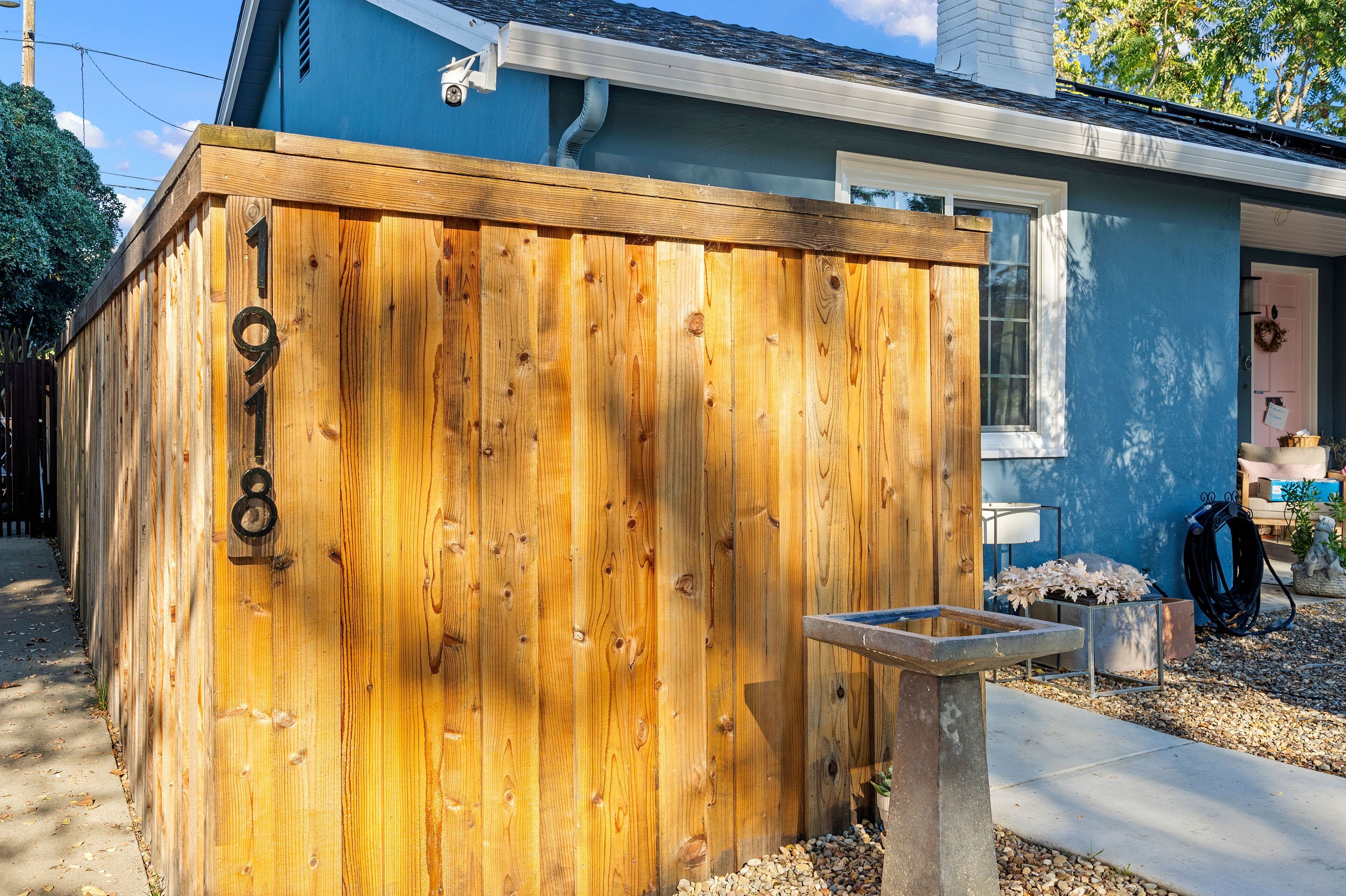 A wooden fence with the number 918, a concrete planter, and a house with a blue exterior and a white window.
