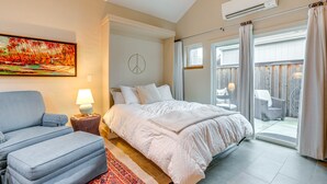 A bedroom with a bed, a chair, a lamp, a painting, and a view to the outside.