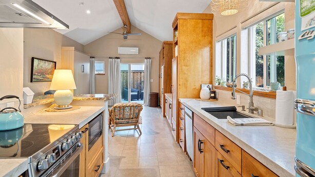 A modern kitchen with a stove, sink, and wooden cabinets. There is a chair and a table with a lamp.