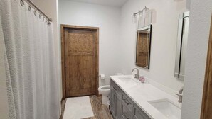 Une petite salle de bain avec une porte en bois, un lavabo blanc, un miroir et un rideau de douche.