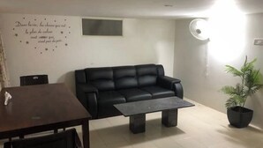 A modern living room with a black leather sofa, a dark coffee table, and a potted plant. A wall decor with a French quote is visible. - Z2 - Maison de ZEN 2, For Serenity, Bliss & Relaxation (Murugeshpalya)