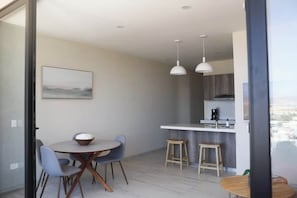 A modern kitchen with a white countertop, two stools, and a hanging light fixture.