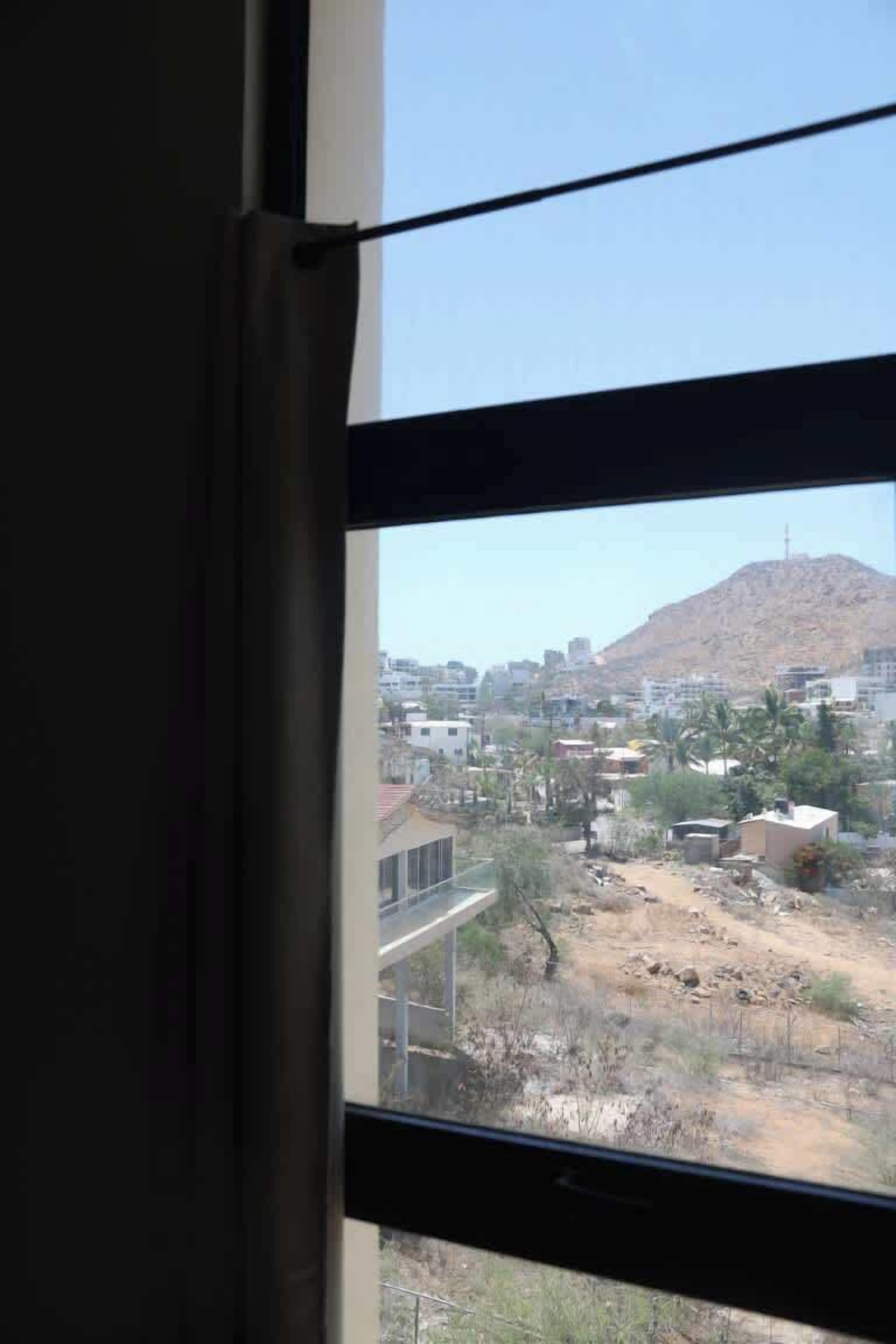 A window view of a cityscape with buildings, a hill, and a clear sky.