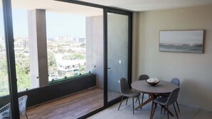 A balcony with a view of buildings and greenery, a dining table with chairs, and a painting on the wall. - Ocean's Point by Baja Toms (Cabo San Lucas)