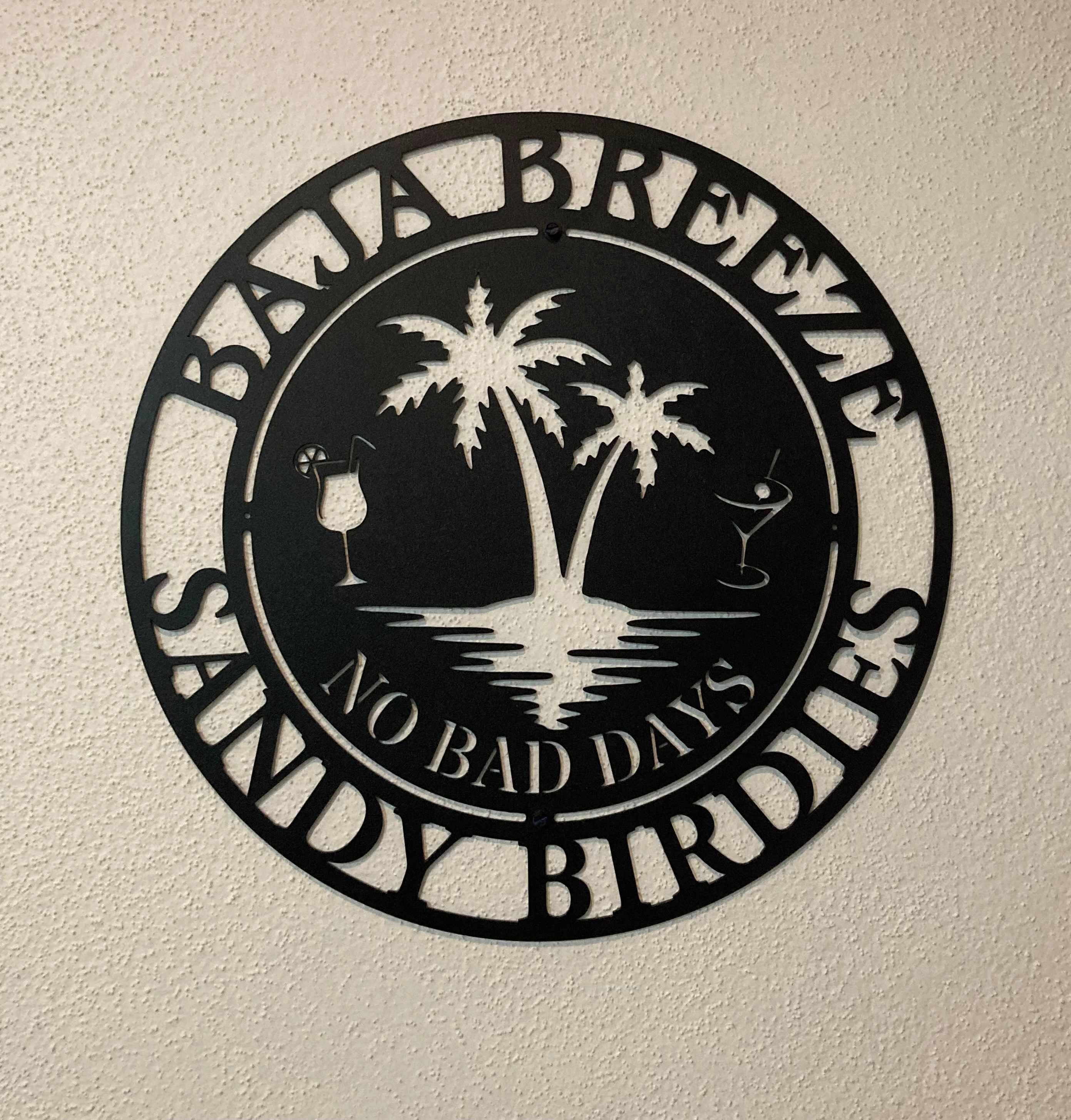 A circular sign with palm trees and a beach scene, featuring the text 'Baja Breeze Sandy Birdies' and 'No Bad Days'.