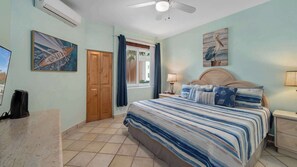 A bedroom with a bed, a nightstand, a ceiling fan, and artwork on the walls.
