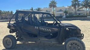 Ein schwarzes Honda ATV auf einem sandigen Strand, im Hintergrund sind Gebäude zu sehen.