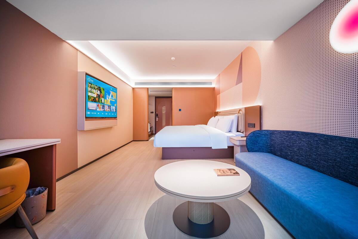 Ein modernes Hotelzimmer mit einem Bett, einer Couch, einem runden Tisch und einem an der Wand befestigten Fernseher.
