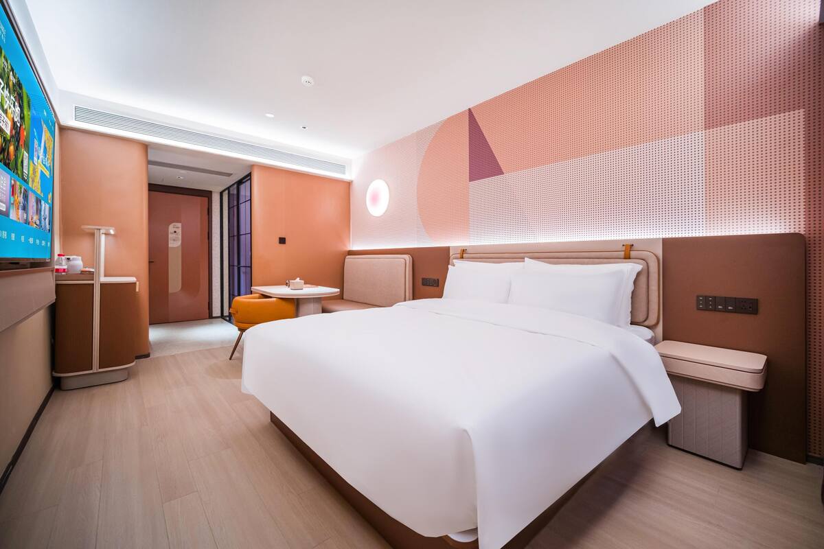 Ein modernes Hotelzimmer mit einem großen Bett, Nachttischen, einer kleinen Sitzecke und einem Fernseher.