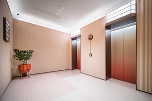 A modern elevator area with two elevators, a potted plant, and a wall-mounted clock. - Orange Hotel Guangzhou Yuexiu Park (Guangzhou)