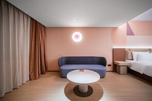 Quarto de hotel moderno com uma mesa redonda, um sofá, uma cama e um candeeiro fixado na parede.