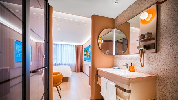 A modern hotel bathroom with a sink, mirror, and toilet. There is a shower area with a handheld showerhead and a towel rack. The room has a large mirror and a window with curtains. - Orange Hotel Guangzhou Yuexiu Park (Guangzhou)