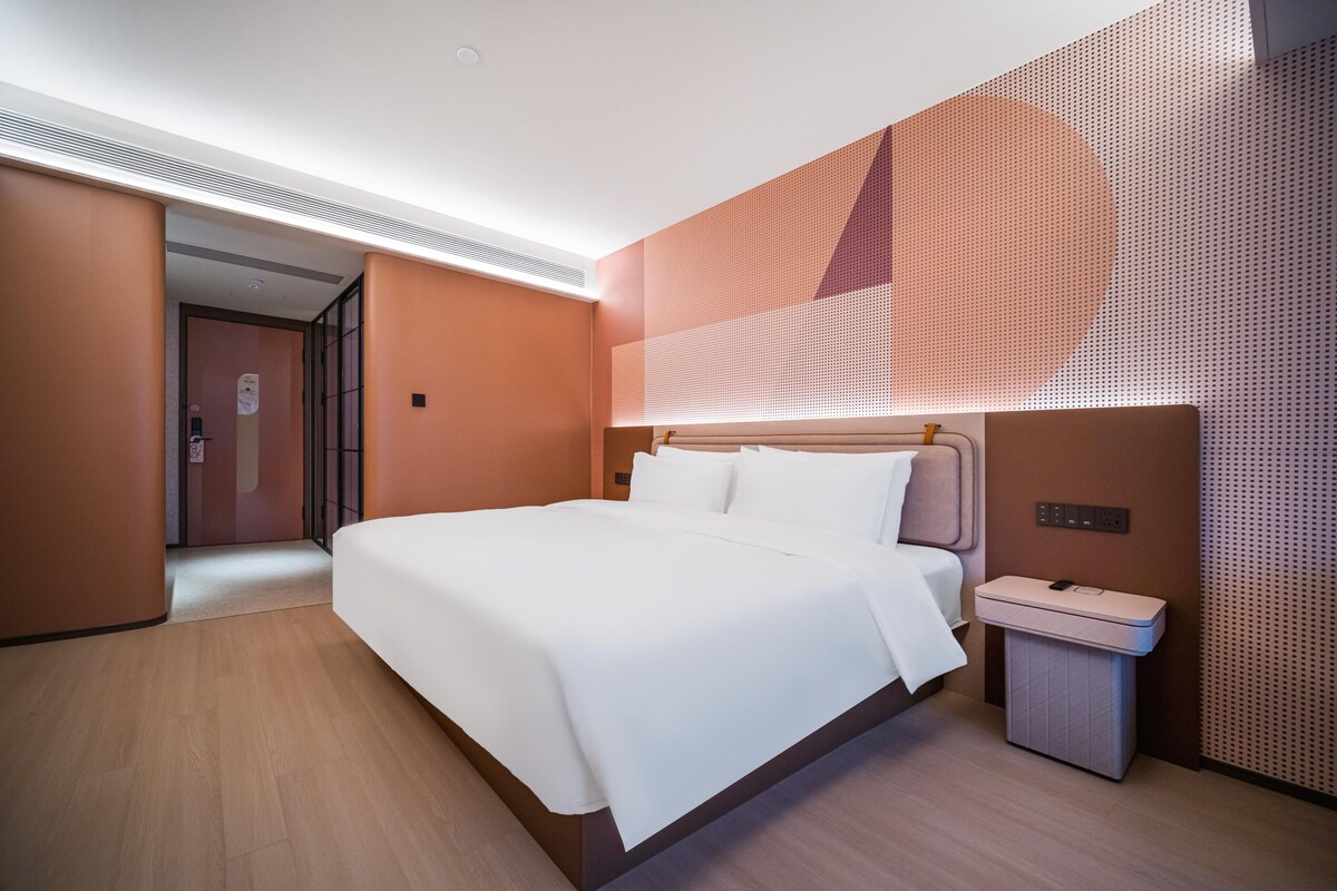 Quarto de hotel moderno com uma cama grande, uma mesinha de cabeceira e um painel fixado na parede.