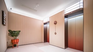 Un área moderna de ascensores con dos elevadores, una planta en maceta y un reloj en la pared.