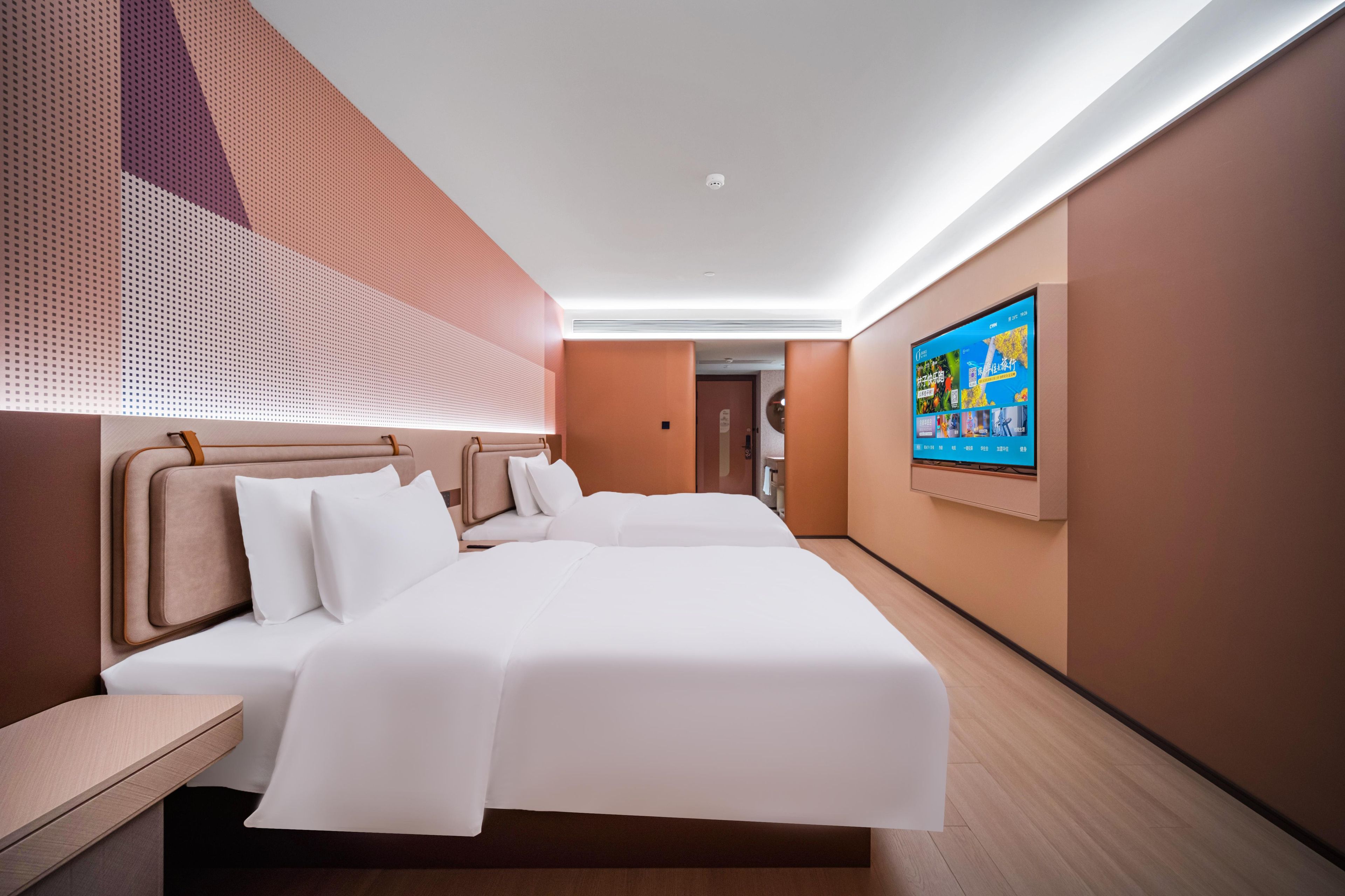 Une chambre d’hôtel moderne dotée d’un grand lit, d’un téléviseur fixé au mur et d’un plafond orné d’un motif géométrique.