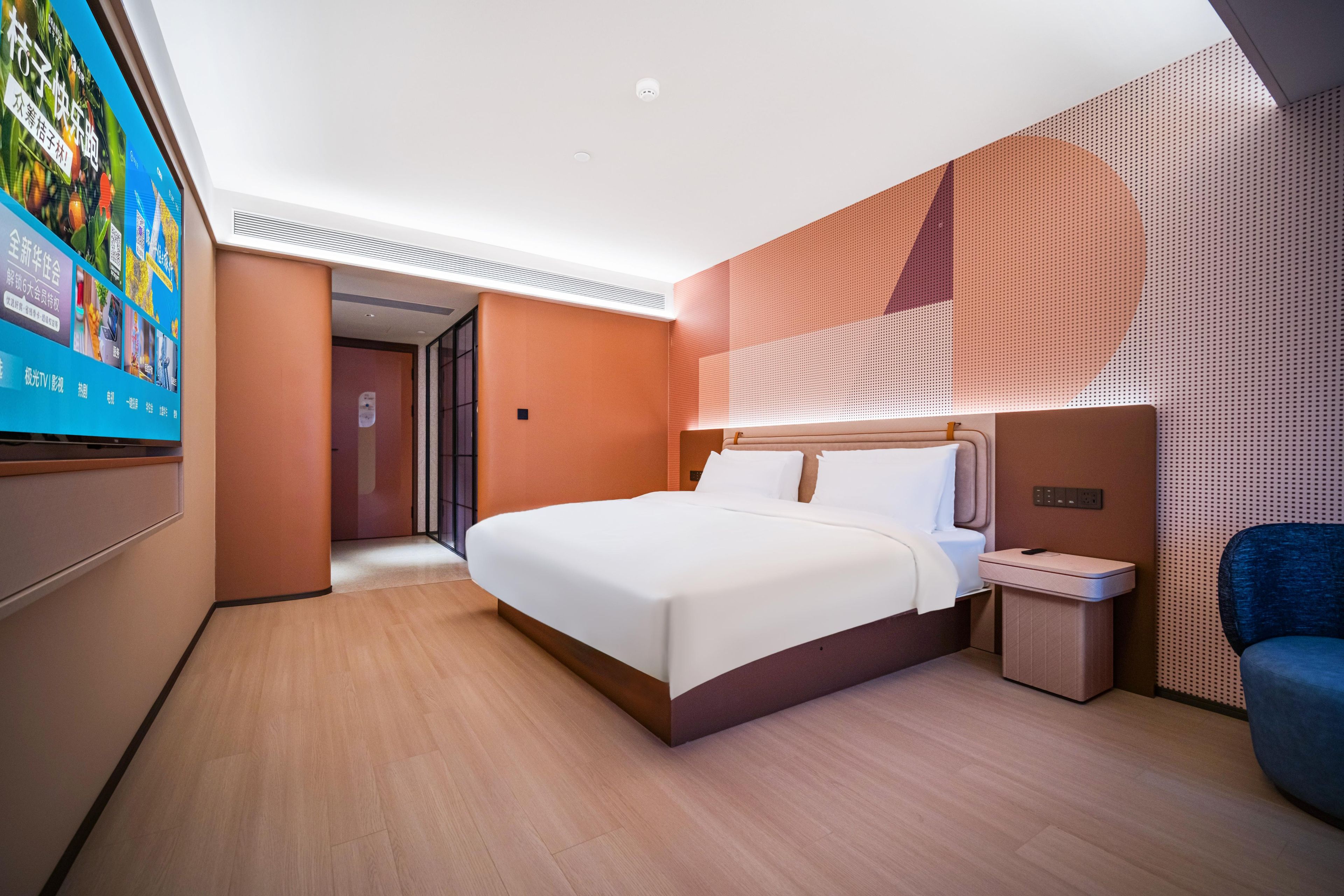 A modern hotel room with a large bed, a bedside table, a chair, and a TV mounted on the wall.