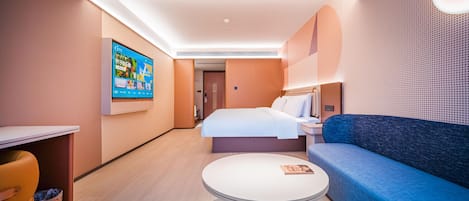 A modern hotel room with a bed, a sofa, a round table, and a TV mounted on the wall.