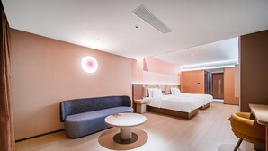 Una habitación de hotel moderna con un sofá azul, una mesa redonda, una cama con ropa de cama blanca y una pared decorativa de madera.