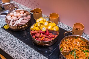 A buffet table with various dishes including sausages, corn on the cob, sweet potatoes, and noodles. - Orange Hotel Guangzhou Yuexiu Park (Guangzhou)