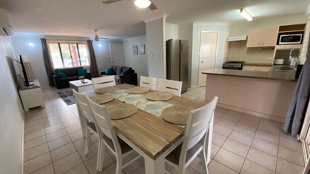 Une cuisine moderne avec un coin repas, comprenant une table en bois, des chaises blanches et un four à micro-ondes encastré.
