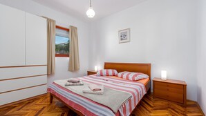 Un dormitorio con cama, mesitas de noche de madera, una ventana con cortinas, un cuadro en la pared y un suelo con estampado de espiga.