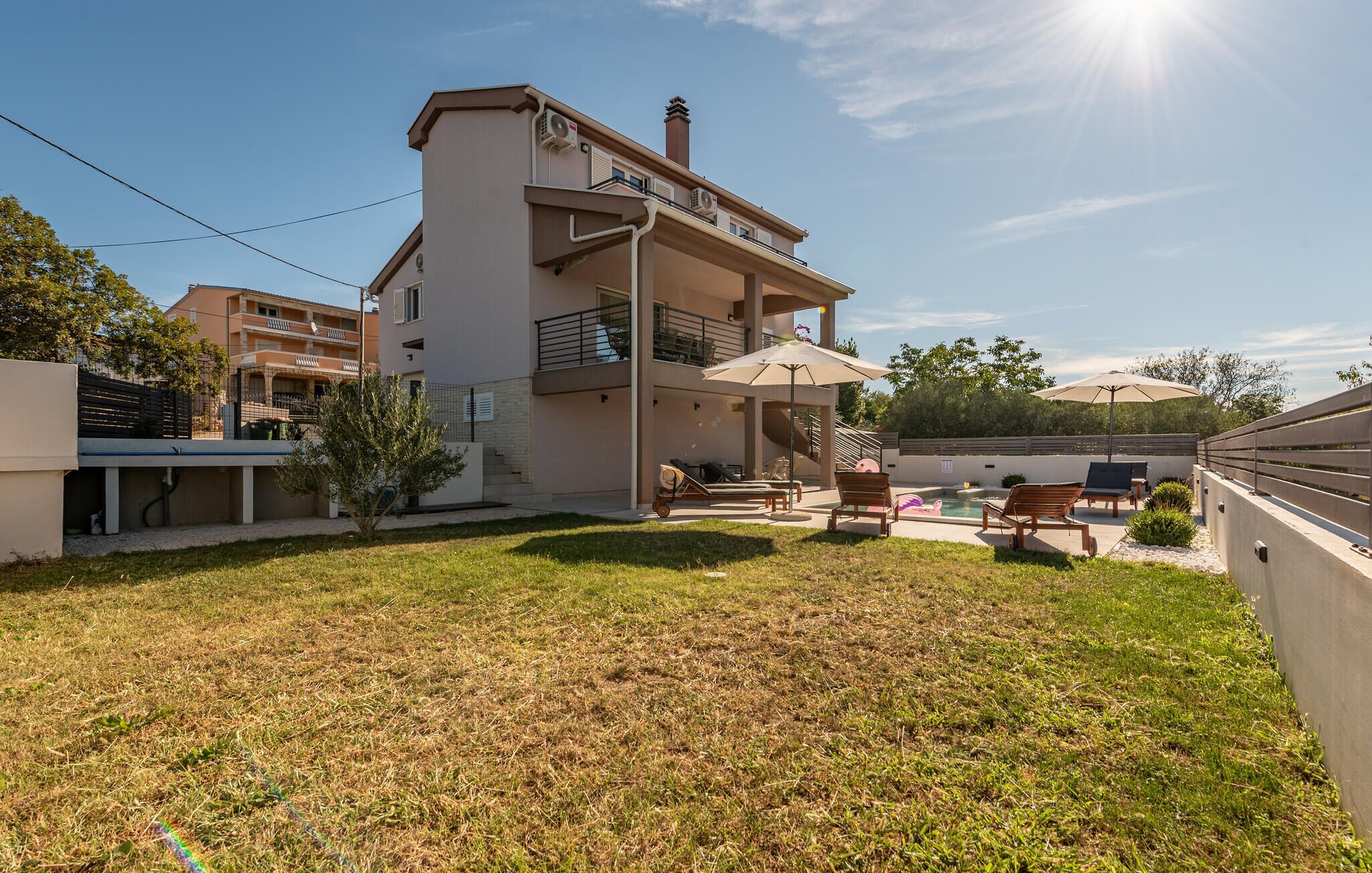 Un bâtiment moderne à deux étages, doté d’un toit plat, d’un balcon et d’un espace extérieur abrité avec des parasols, aménagé pour accueillir des clients.