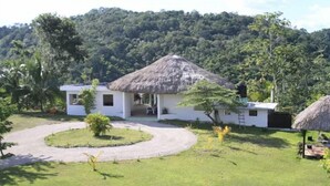 A white building with a thatched roof, surrounded by a well-maintained garden with a circular pathway. - Mayan World Adventures (Estero Franco)