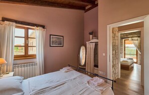A bedroom with a bed, a radiator, a window with curtains, a framed picture, and a mirror.