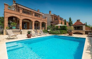 A poolside area with a brick house, outdoor seating, and a barbecue area.