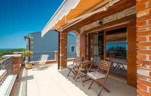 A balcony with a table and chairs, a bottle of wine, and a view of the sea.