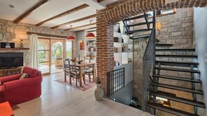 A spacious living area with a stone fireplace, a red sofa, a dining table, and a staircase with a metal railing. - Awesome home in Kastelir (Kastelir)