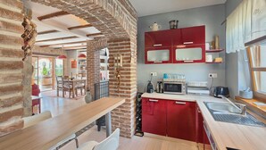 A modern kitchen with red cabinets, a wooden dining table, and a brick accent wall. - Awesome home in Kastelir (Kastelir)