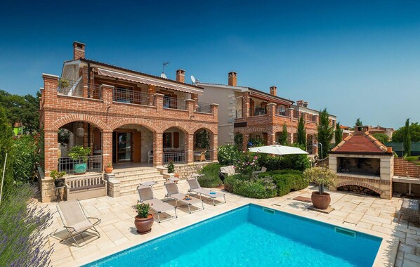 A two-story brick house with a swimming pool, outdoor seating, and a barbecue area.