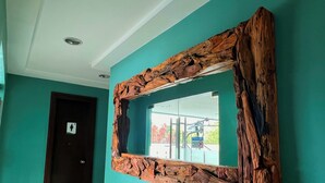 Une pièce aux murs de couleur turquoise, avec un miroir encadré en bois, une porte portant l’indication « toilettes pour femmes » et une fenêtre donnant sur un immeuble et de la verdure.